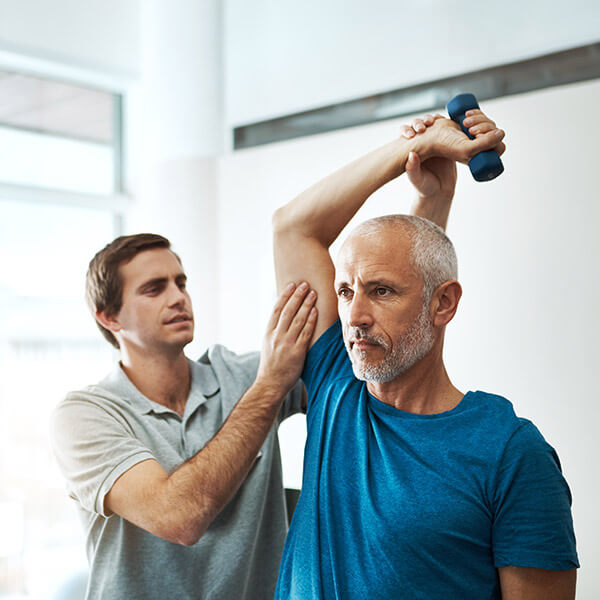 man holding weight in the air being assisted by therapist